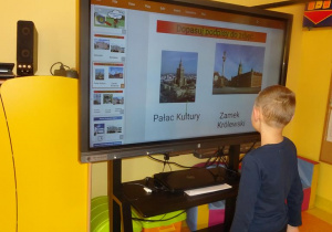 Chłopiec stoi pod ekranem mobilnym, dopasowuje podpis do zdjęcia.
